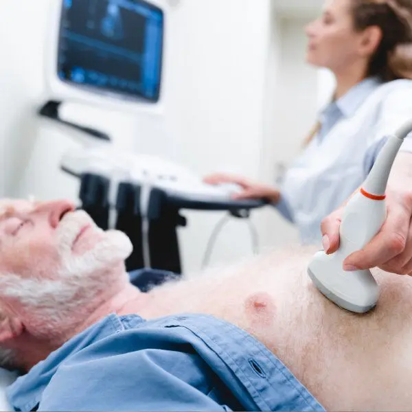 Un homme senior à la barbe blanche, un docteur en arrière plan lui fait une échographie cardiaque.