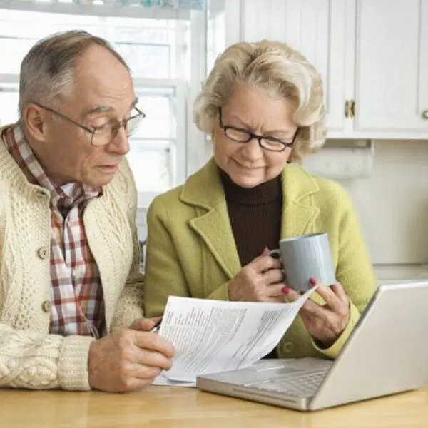 Un couple de seniors discutent d'un document imprimé, assis devant un ordinateur portable.