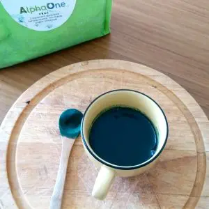 Une tasse remplie d'algue de Klamath Alpha ONE, une petite cuillère en bois remplie d'algue en poudre.