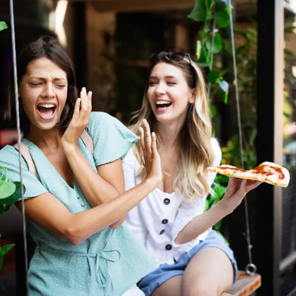 Une jeune femme propose une pizza à une autre qui la refuse à cause de son intolérance alimentaire au gluten et au lactose.
