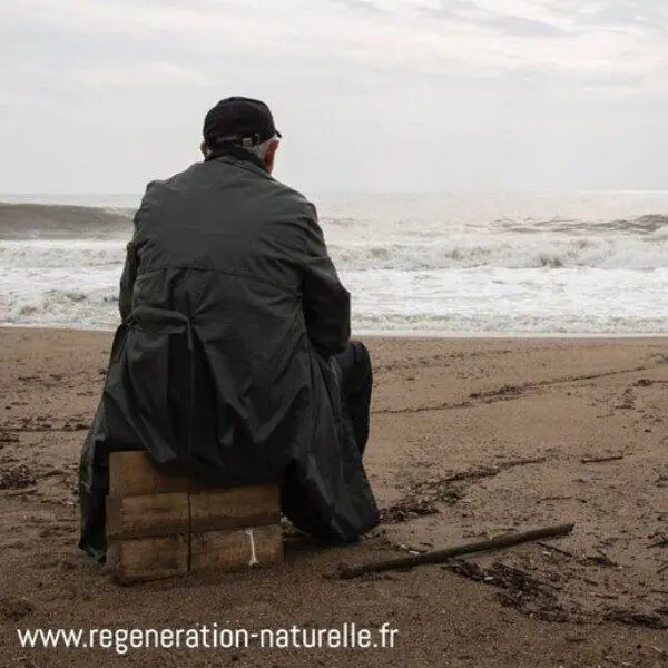 Un homme de dos assis sur la plage regarde l'océan.
