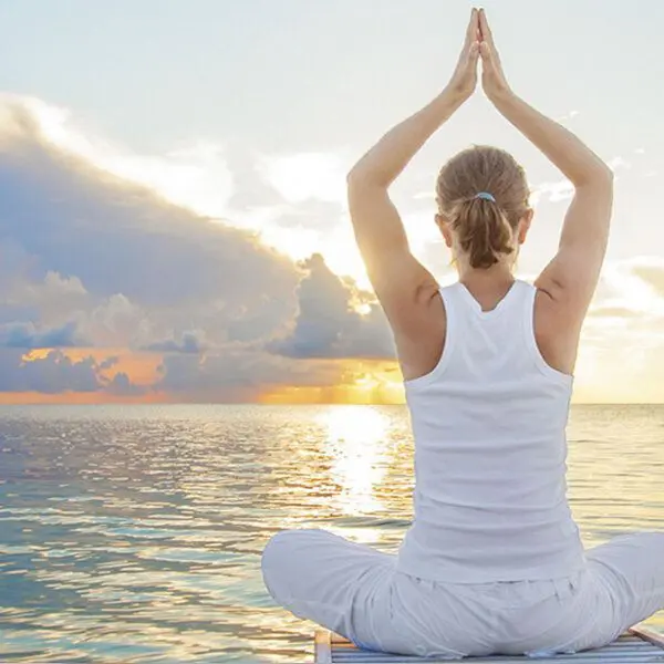 Une femme médite devant la mer au lever de soleil.