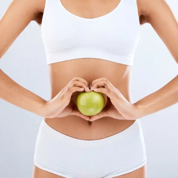 Une femme en sous-vêtements blancs tient une pomme verte devant son estomac.