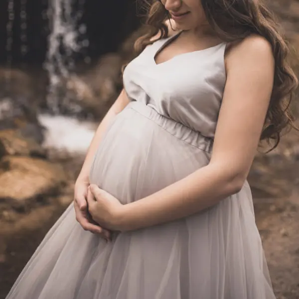 Une femme enceinte se tient le ventre dans un décor de forêt.