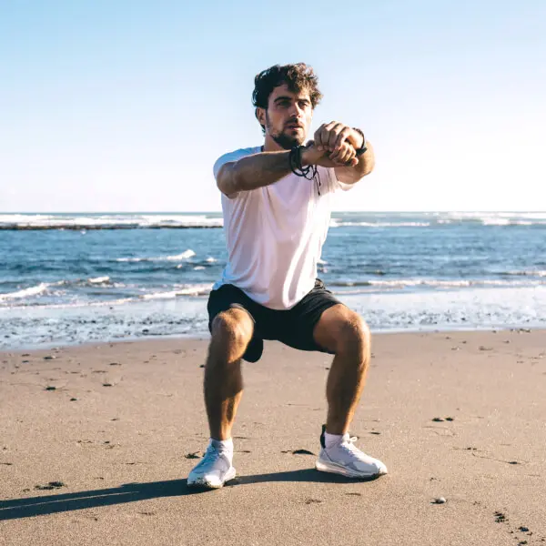 Un homme athlétique fait des squats sur une plage ensoleillée.