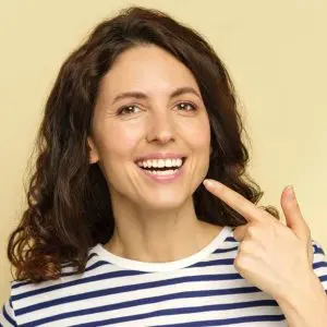 Une femme pointe du doigts ses dents blanches reminéralisées.