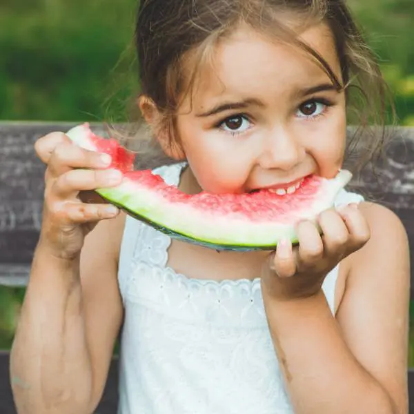 Une petite fille croque dans une pastèque crue.