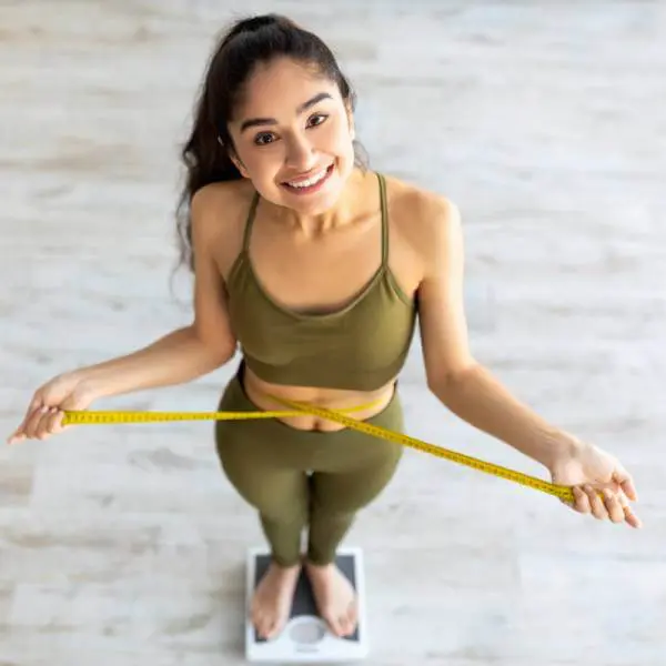 Une jeune femme vue en contre-plongée sur une balance se mesure la taille pour perdre du poids.