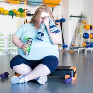 Une jeune femme obèse expérimente une prise de poids, ventre gonflé, fatigue, à la gym.