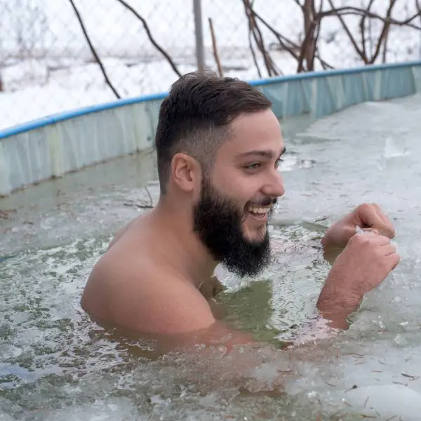 Un jeune homme souriant dans un bain glacé pour accélérer la récupération musculaire.