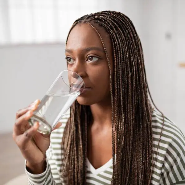Une jeune femme boit un verre d'eau.