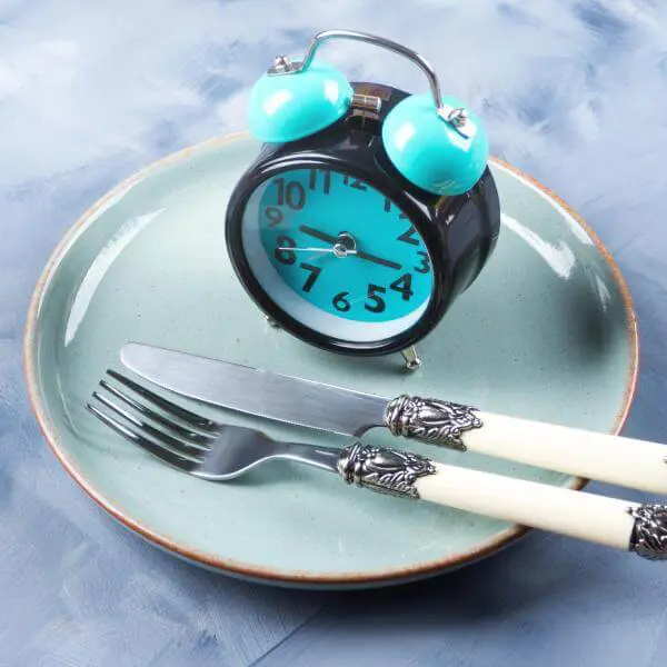 Une assiette vide avec des couverts et une horloge analogique.