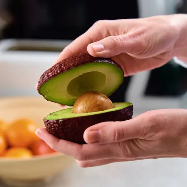 Deux mains tiennent un avocat mûr ouvert en deux.