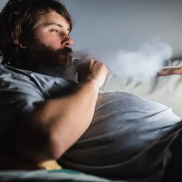 Un homme en surpoids allongé fume une cigarette.