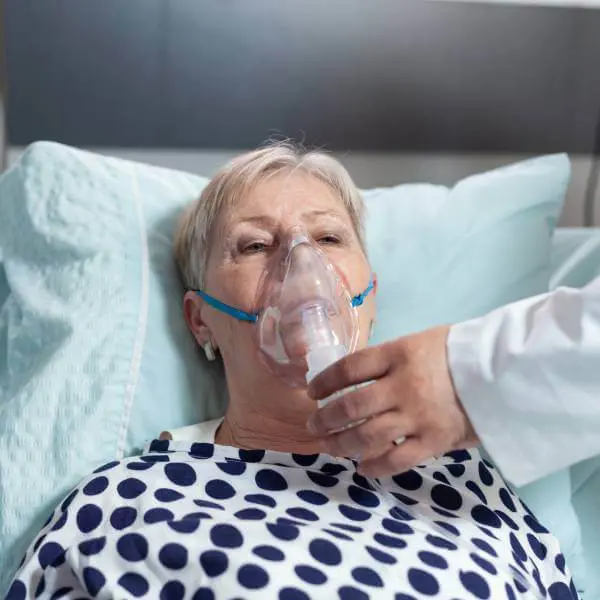 Une dame âgée alitée avec un masque d'oxygène.
