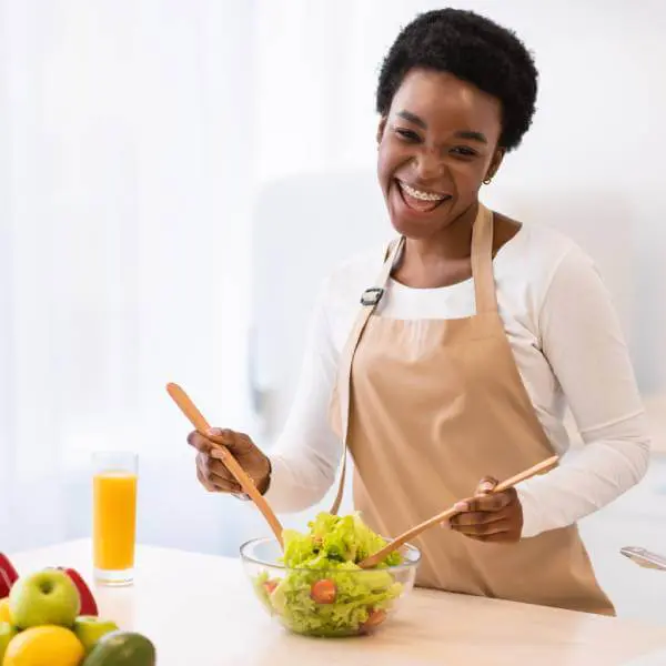 Une femme souriante cuisine avec les 6 meilleurs aliments pour rajeunir la peau.