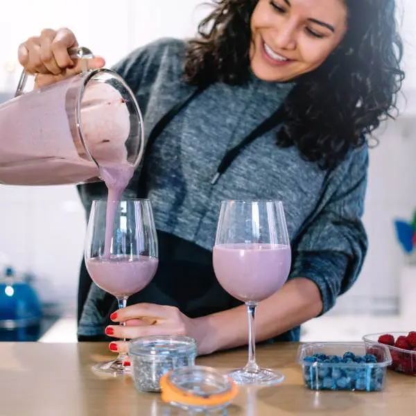 Une femme verse un smoothie aux fruits rouge dans des verres.