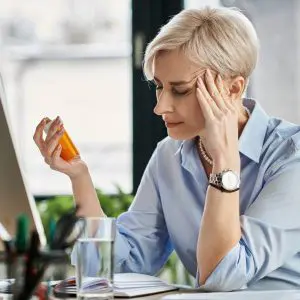 Une dame ménopausée regarde un flacon de granules d'homéopathie.