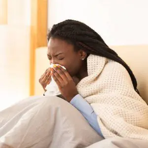 Une jeune femme enrhumée éternue dans un mouchoir.