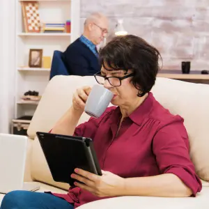 Une dame assise sur son canapé réalise un test d'électrosensibilité sur sa tablette.